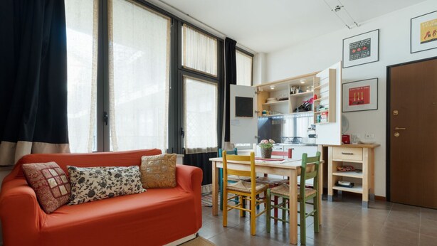 A compact living space with a sofa, dining table, chairs, and a kitchenette. - GuestHost - Cozy Apartment in Milan (Milan)