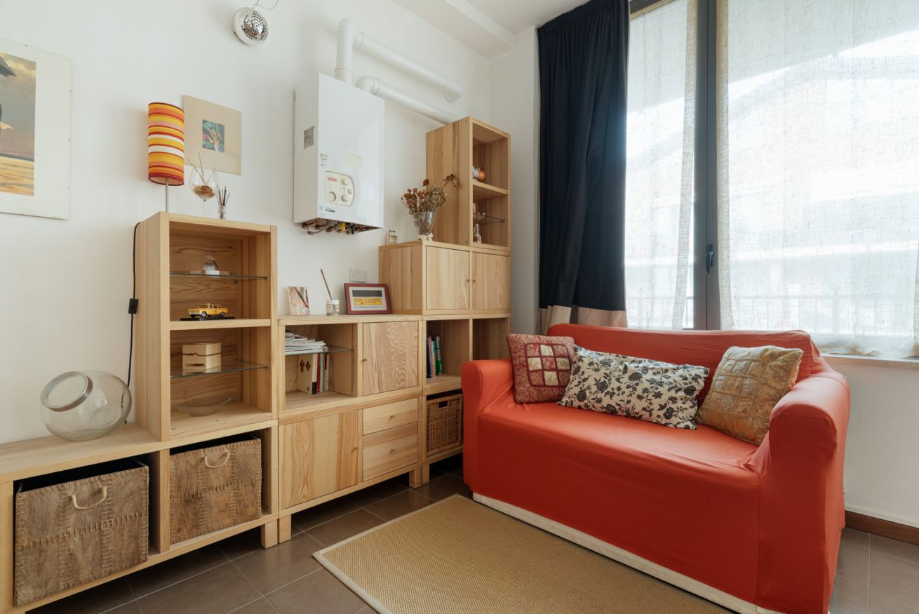 A modern living room with a red sofa, wooden shelving, and a large window with curtains.