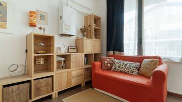 A modern living room with a red sofa, wooden shelving, and a large window with curtains.