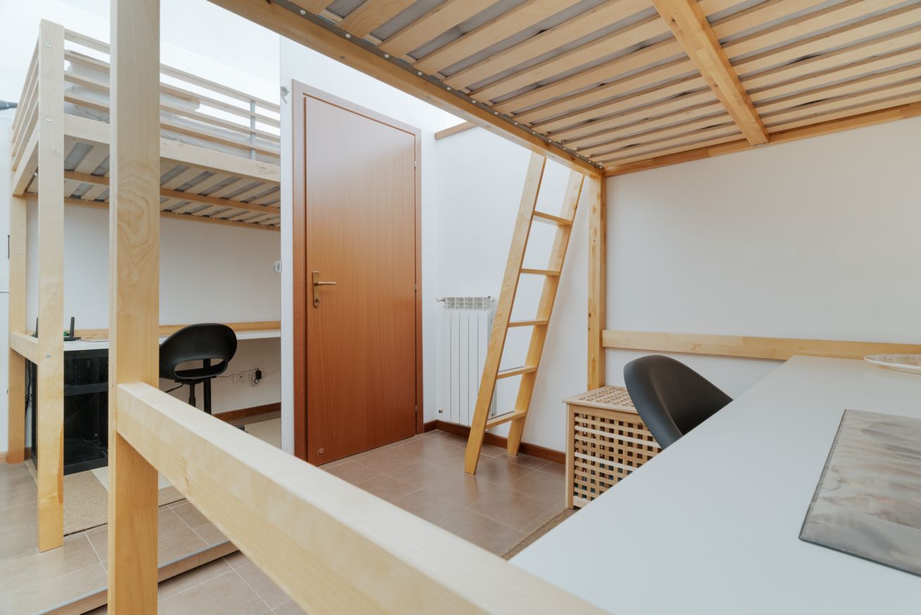A room with a bunk bed, a desk, a chair, and a ladder.