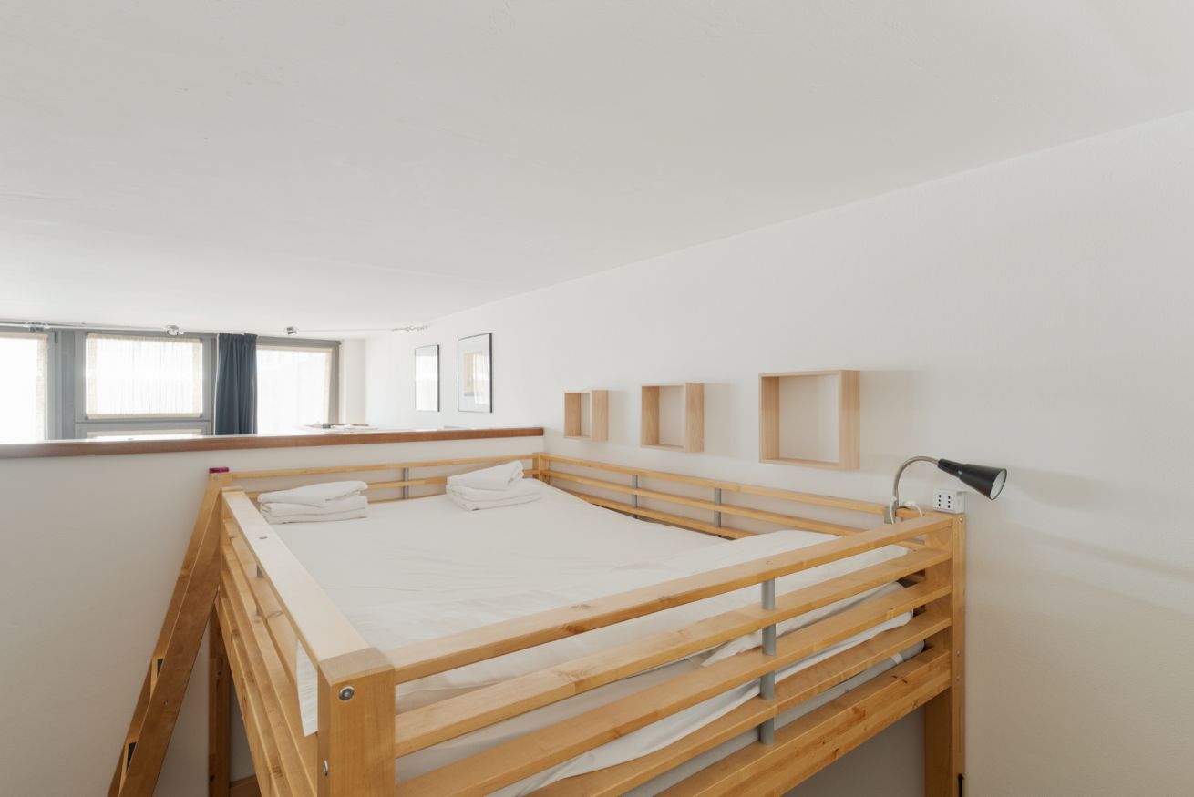 A minimalist bedroom with a wooden bunk bed, a bedside lamp, and a window with curtains.