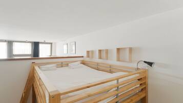 A minimalist bedroom with a wooden bunk bed, a bedside lamp, and a window with curtains.