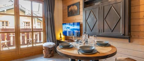 A dining area with a round table, wooden stools, and a television on the wall.