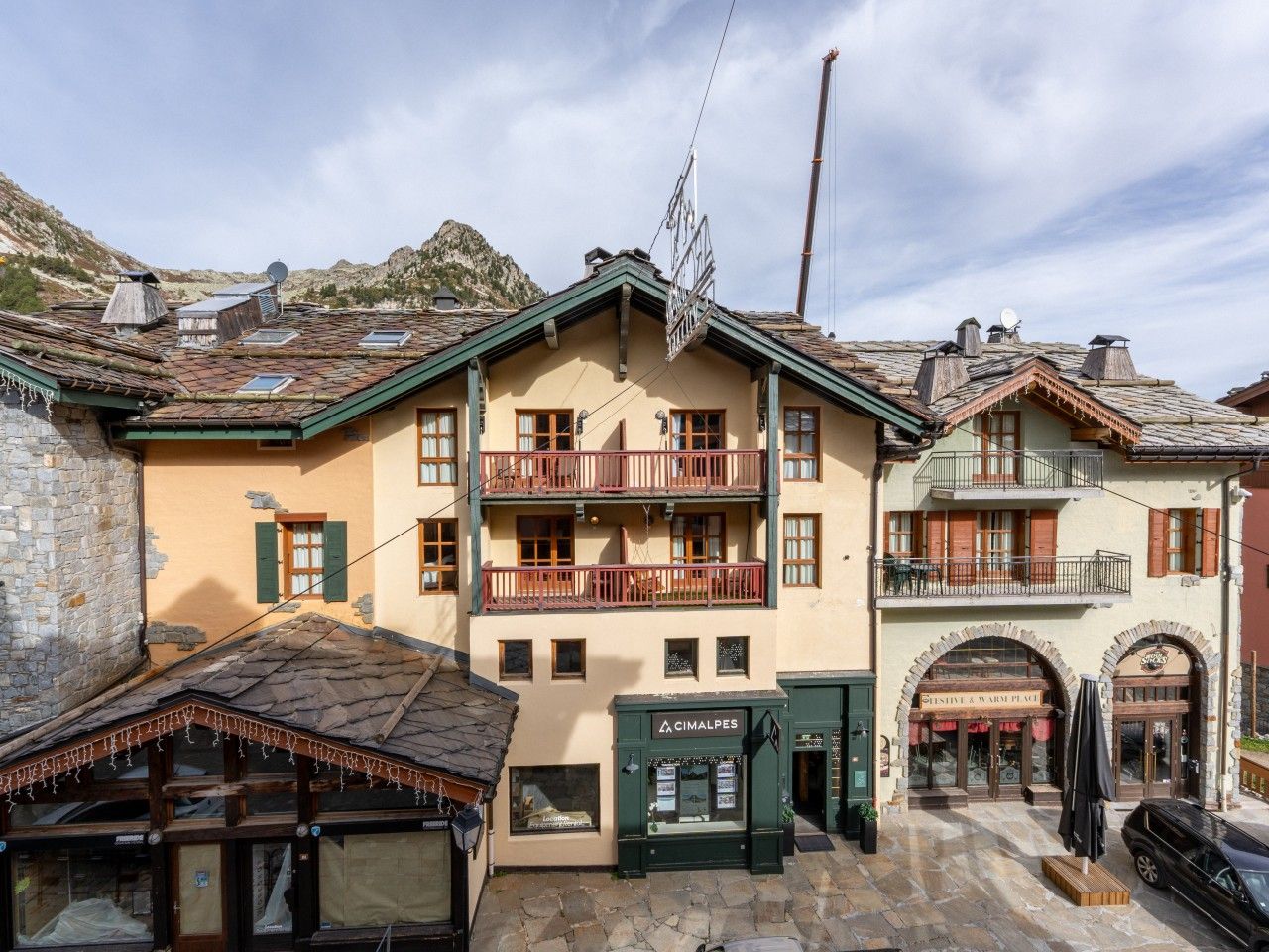 Un edificio tradicional con balcón, una tienda en la planta baja y una montaña al fondo.