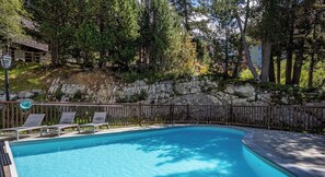 A swimming pool with lounge chairs, surrounded by a stone wall and trees. - Cosy 2 Bed Apartment - Arc 1950 - Auberge Jerome (Bourg-Saint-Maurice)