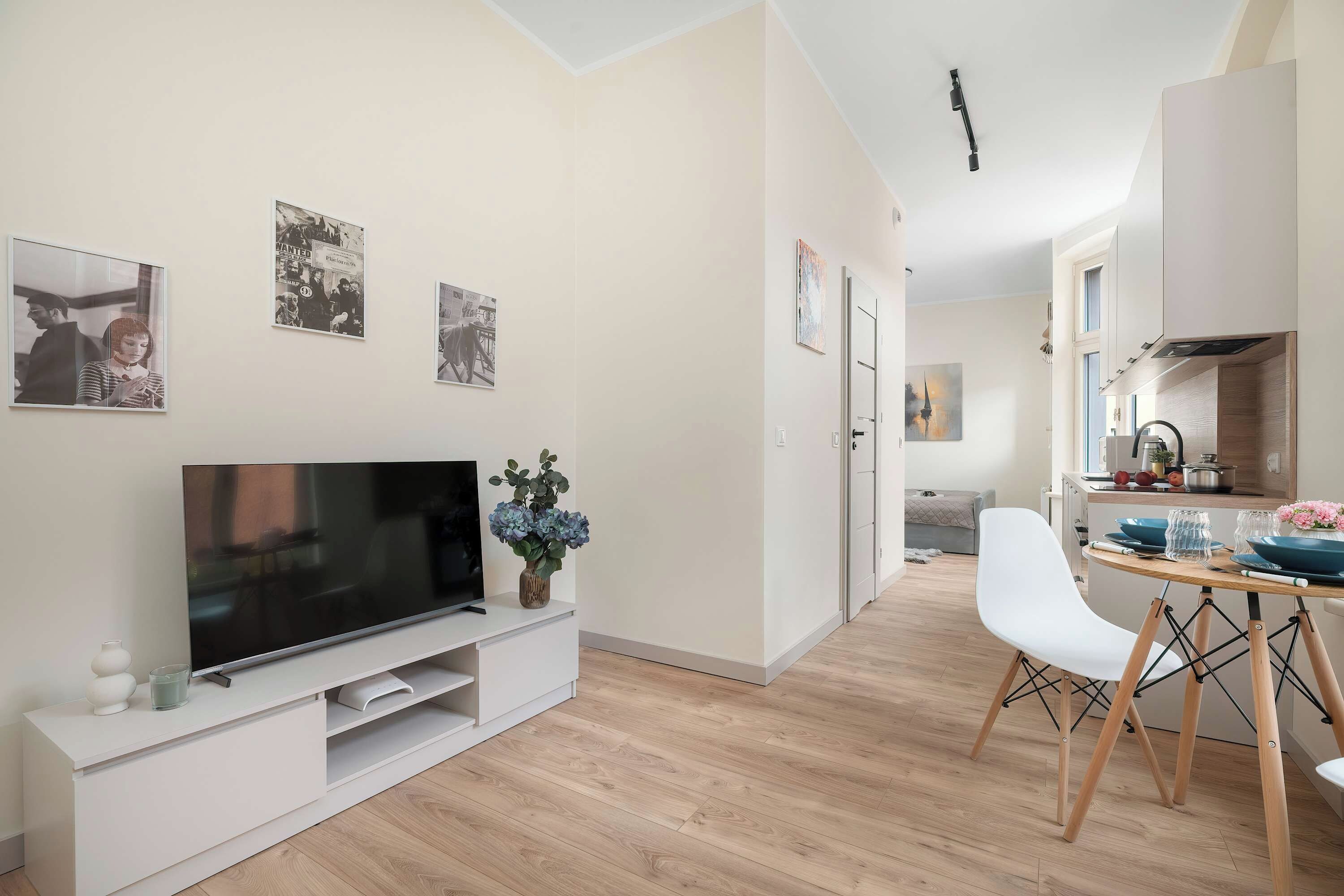 En moderne stue med et fladskærms-TV, et spiseområde med et træbord og stole, og et køkken i baggrunden.