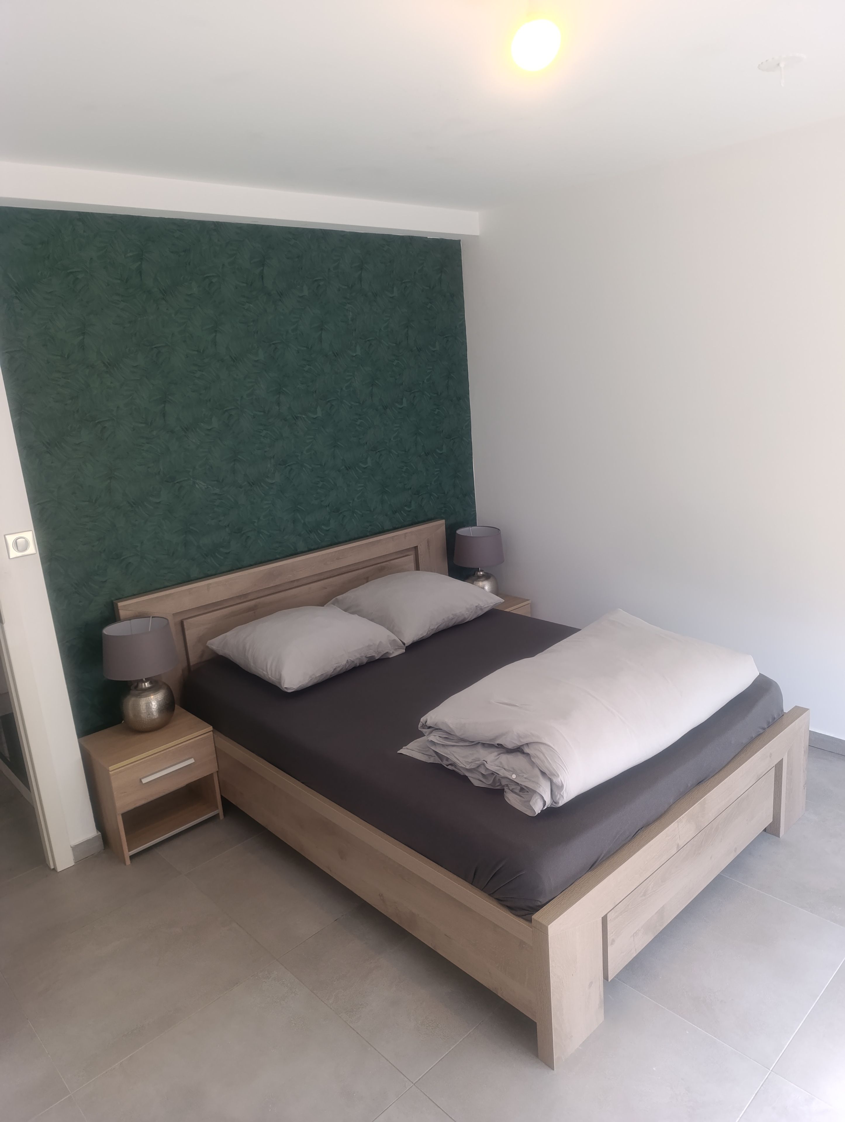 A bedroom with a bed, two bedside tables, a lamp, and a green textured wall.