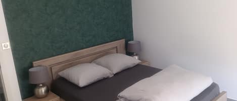 A bedroom with a bed, two bedside tables, a lamp, and a green textured wall.