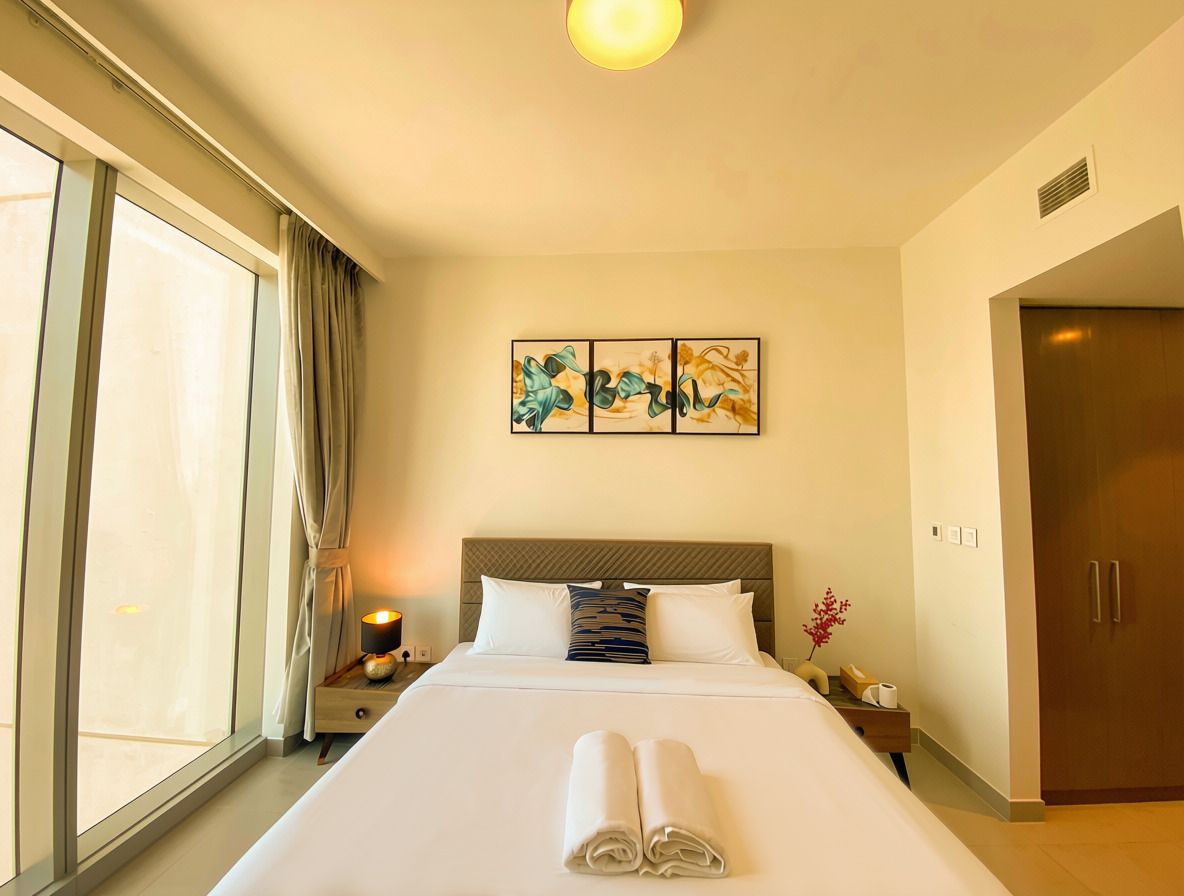 A hotel room with a large bed, a bedside table with a lamp, a wall-mounted artwork, and a door.