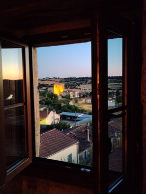 A room with a window overlooking a village at dusk.