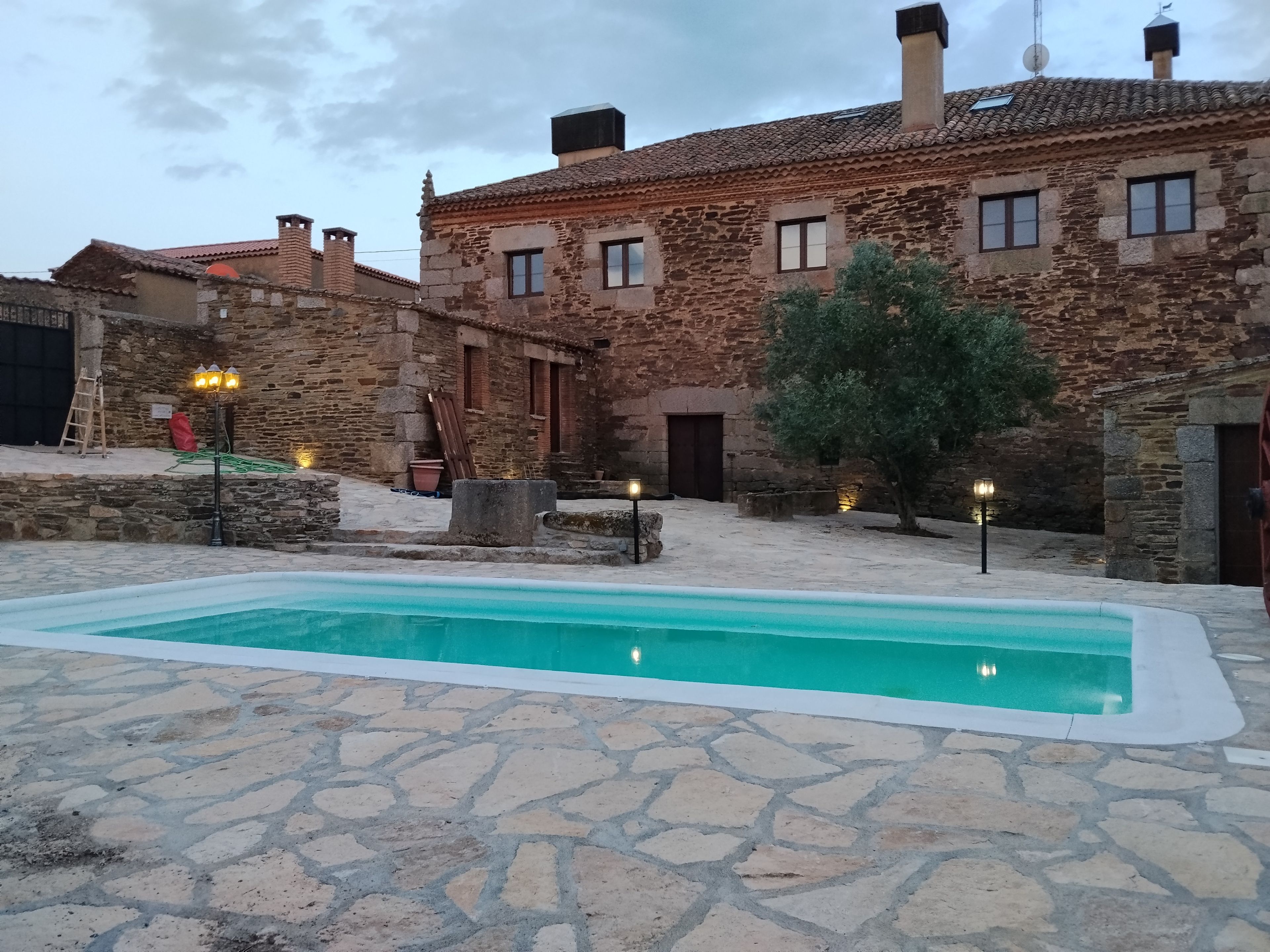 Una piscina de piedra rodeada por un patio con muros de piedra y un edificio tradicional con varias chimeneas.