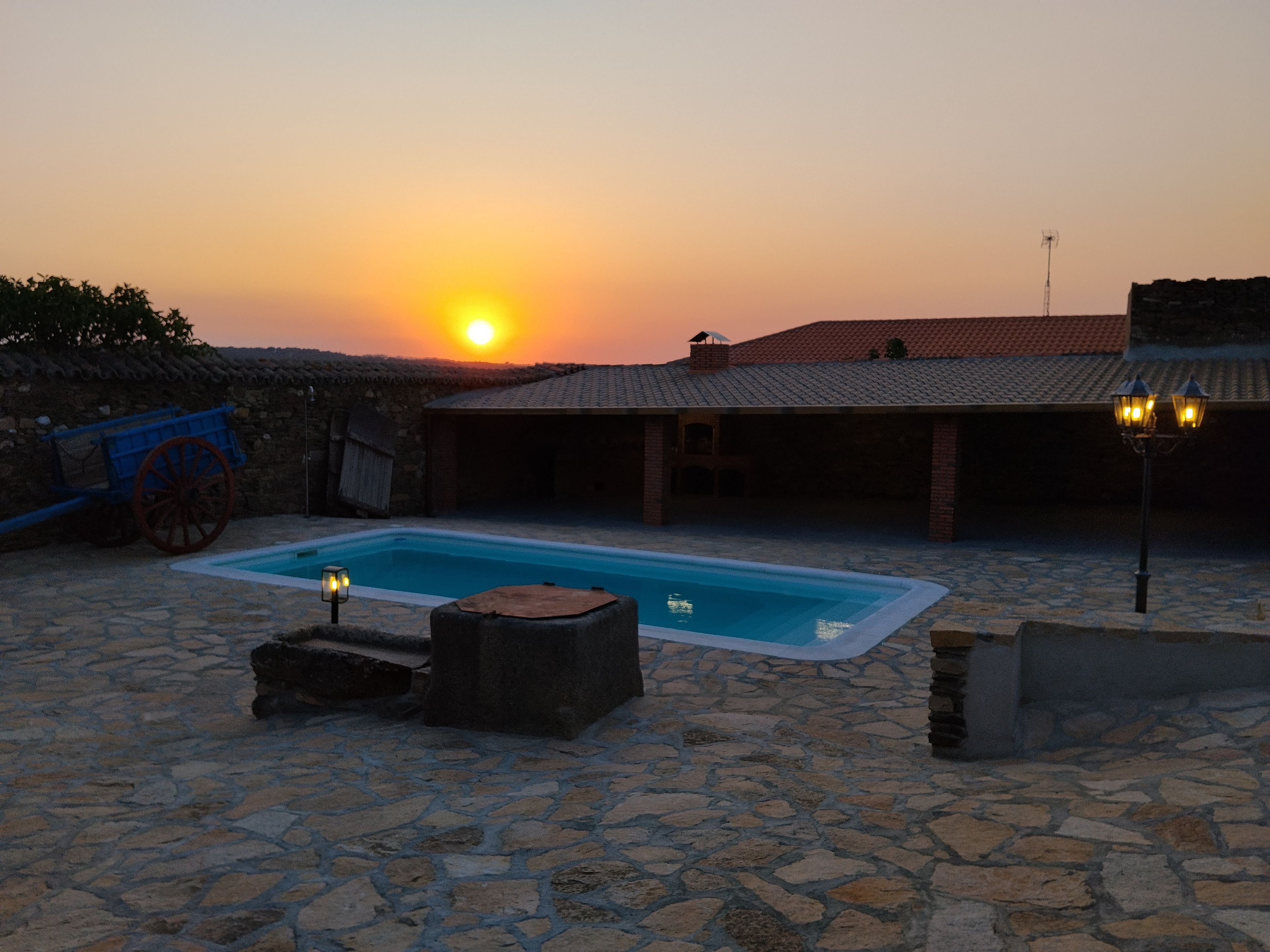 A stone pool with a sunset in the background, surrounded by stone walls and a building with a tiled roof.