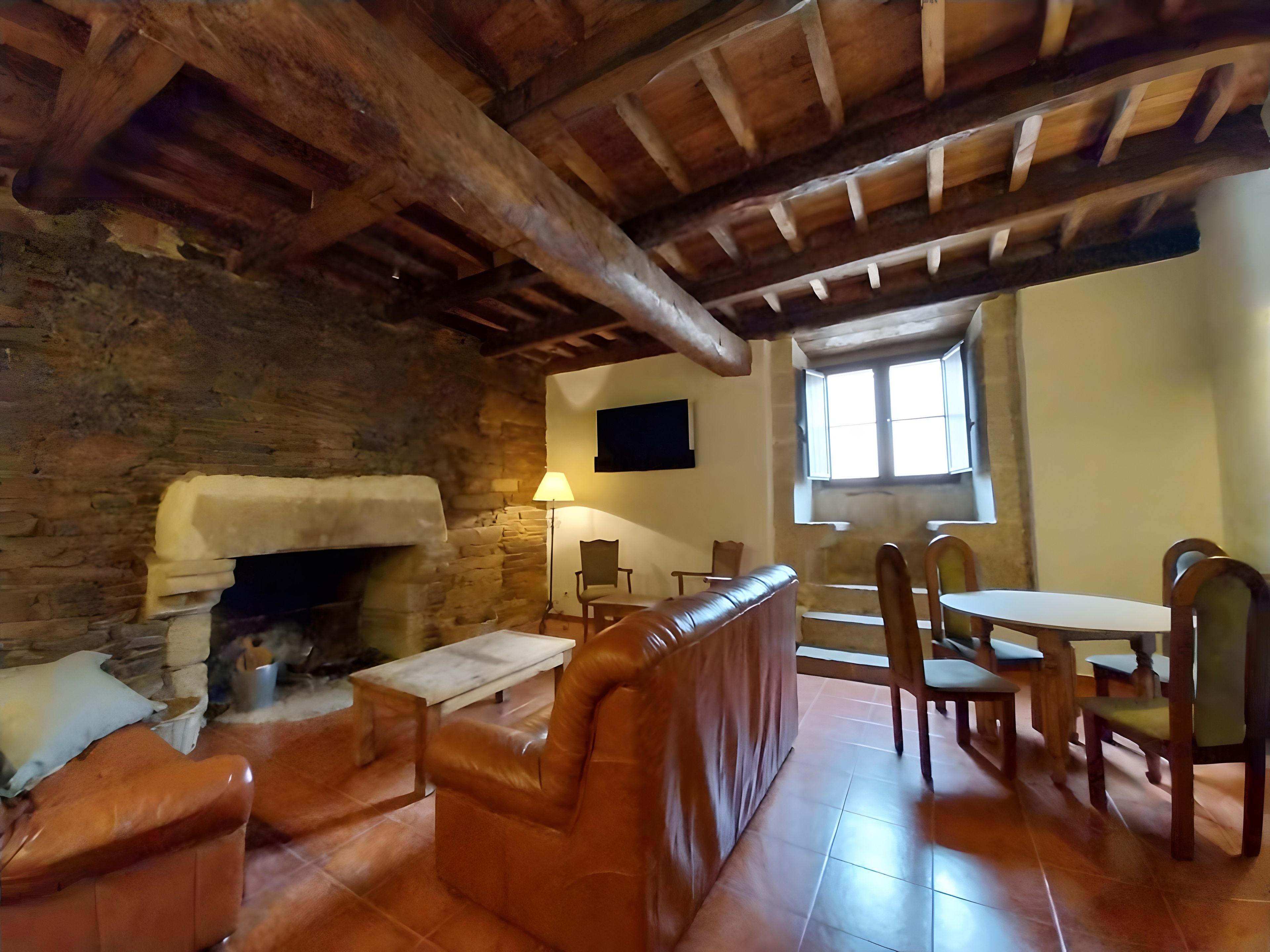 Un interior rústico con chimenea de piedra, asientos de cuero, mesas de madera y pared de piedra.
