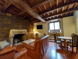 A rustic interior with a stone fireplace, leather seating, wooden tables, and a stone wall.