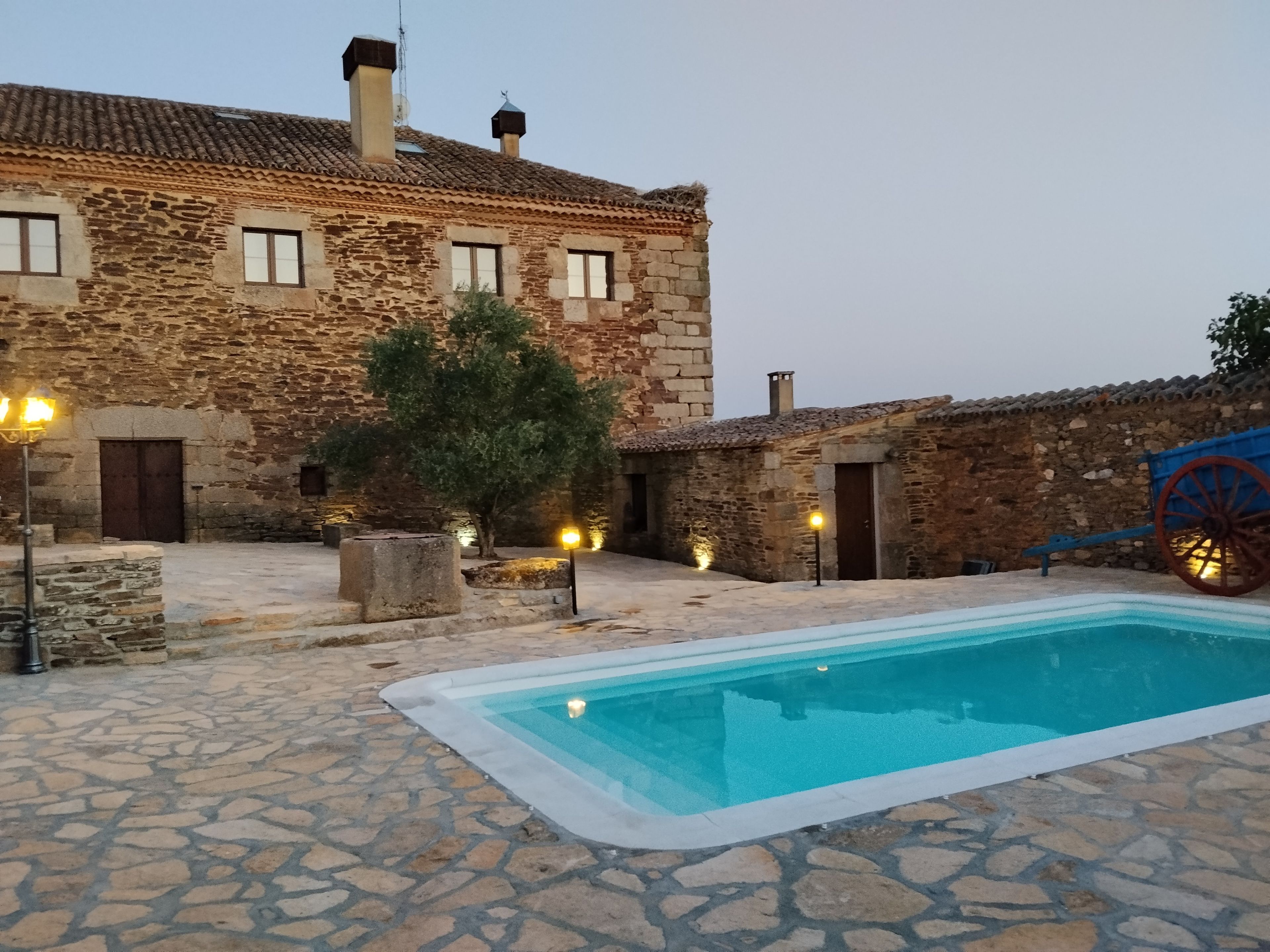 A stone building with a swimming pool, stone walls, and a traditional wheelbarrow.