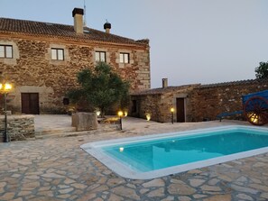 A stone building with a swimming pool, stone walls, and a traditional wheelbarrow.