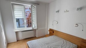 Ein Schlafzimmer mit einem hölzernen Bett, einem Fenster mit Jalousien, einer Heizung und einer Wandleuchte.