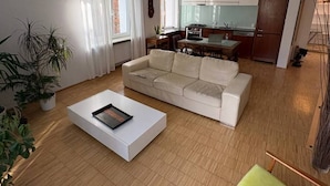 Ein modernes Wohnzimmer mit Sofa, Couchtisch und Essbereich, im Hintergrund eine Küche.