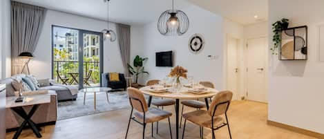 Un salon moderne avec un canapé, une table à manger pour quatre personnes et une grande fenêtre agrémentée de rideaux.
