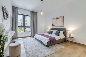 Een moderne slaapkamer met een groot bed, een nachtkastje met lampen, een raam met gordijnen en uitzicht over de stad.