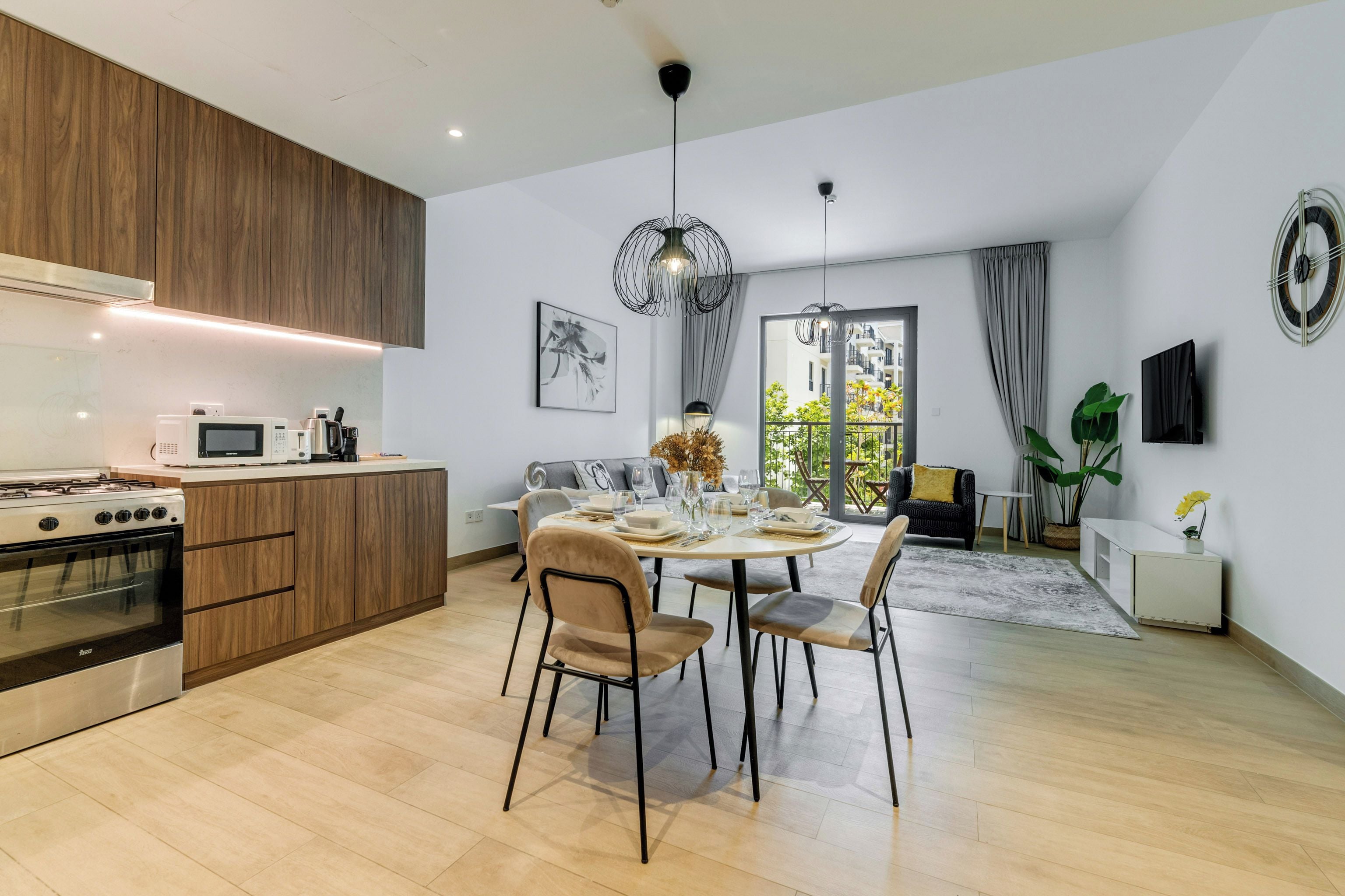 A modern kitchen with built-in appliances, a dining area with a round table and chairs, and a living space with a sofa and a TV.