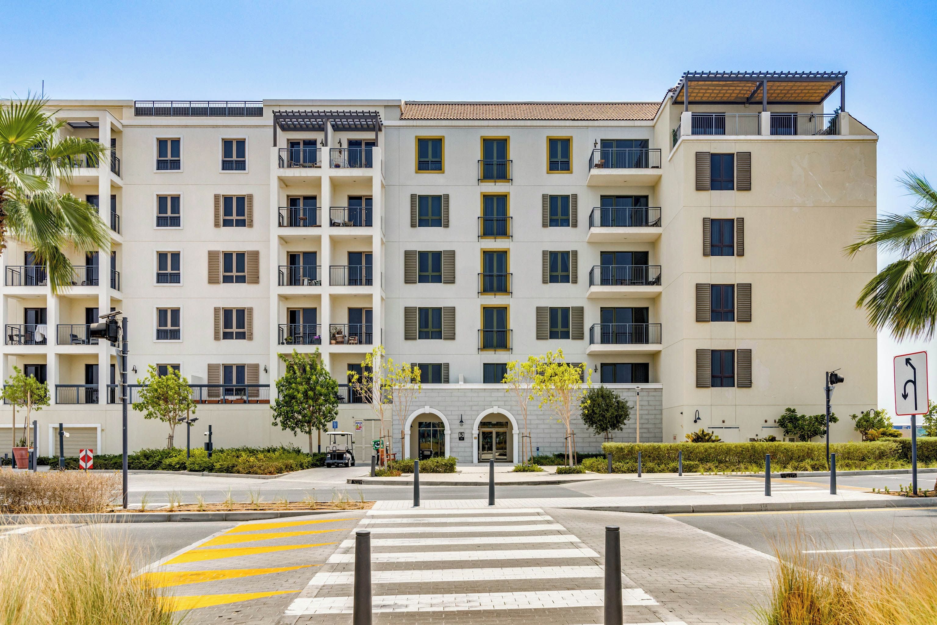 A multi-story residential building with balconies, a gated entrance, and a pedestrian crossing.
