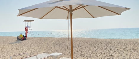A beach with a white umbrella, sun loungers, and a lifeguard chair.