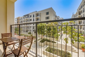 Een balkon met een houten tafel en stoelen, met uitzicht op een woongebied met meerdere appartementencomplexen.
