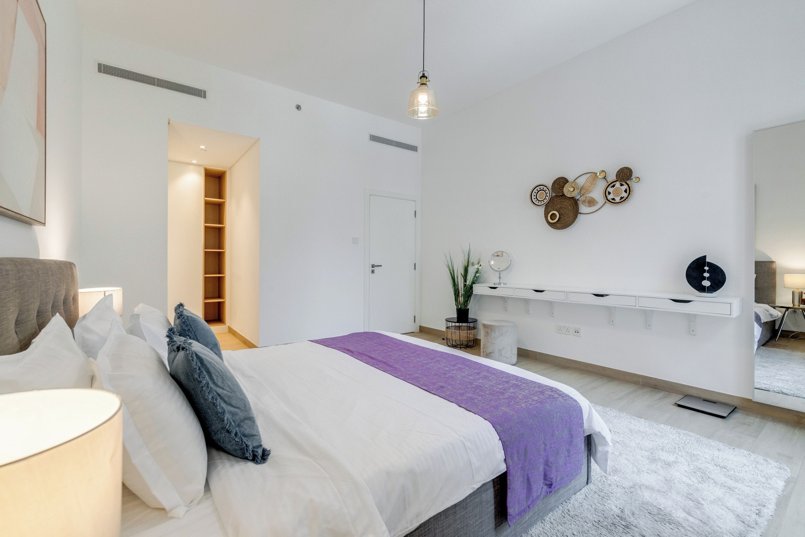 A modern bedroom with a bed, bedside tables, a mirror, and a wall-mounted light fixture.