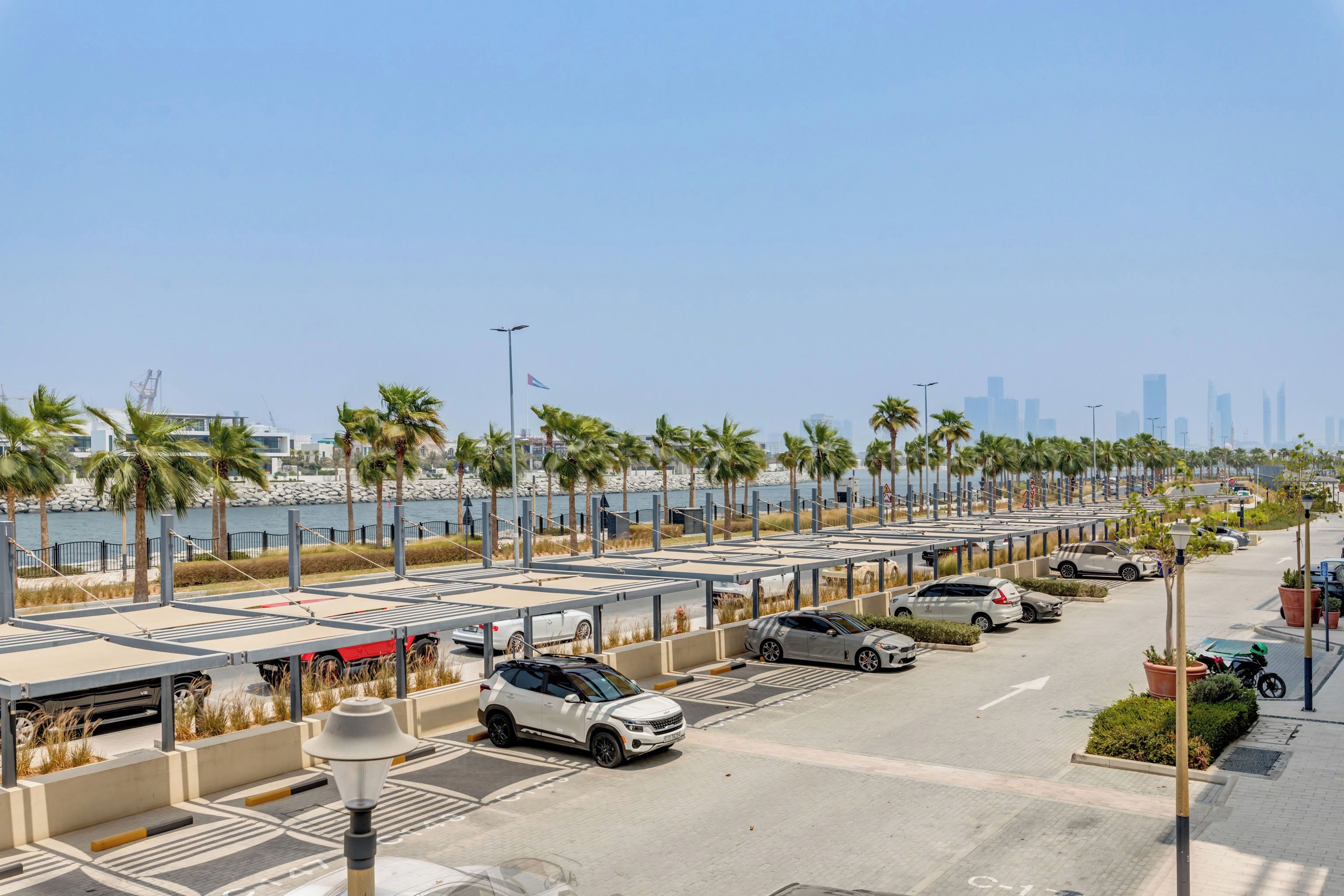 A parking area with multiple cars, palm trees, and a city skyline in the background.