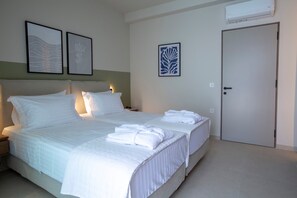 A hotel room with a bed, two bedside tables, a nightstand, a door, and wall-mounted air conditioning unit.