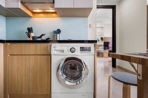 Eine kompakte Küche mit eingebauter Waschmaschine, Holzschränken und einer Arbeitsplatte mit Küchenutensilien.