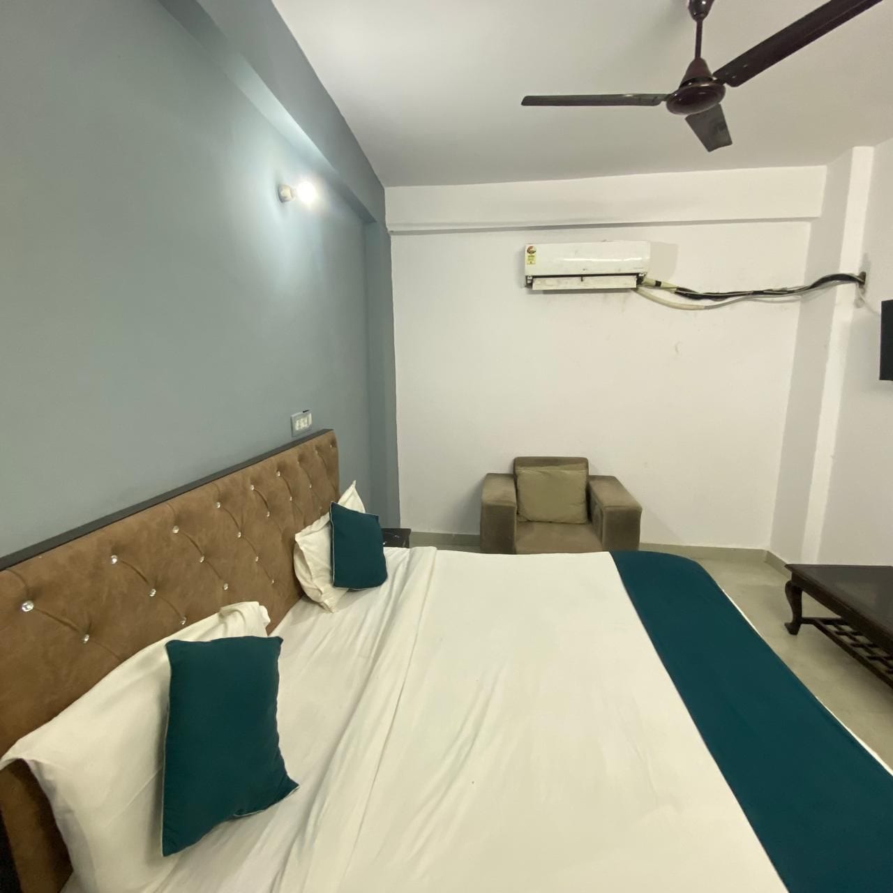 A hotel room with a bed, a chair, a ceiling fan, and an air conditioning unit.
