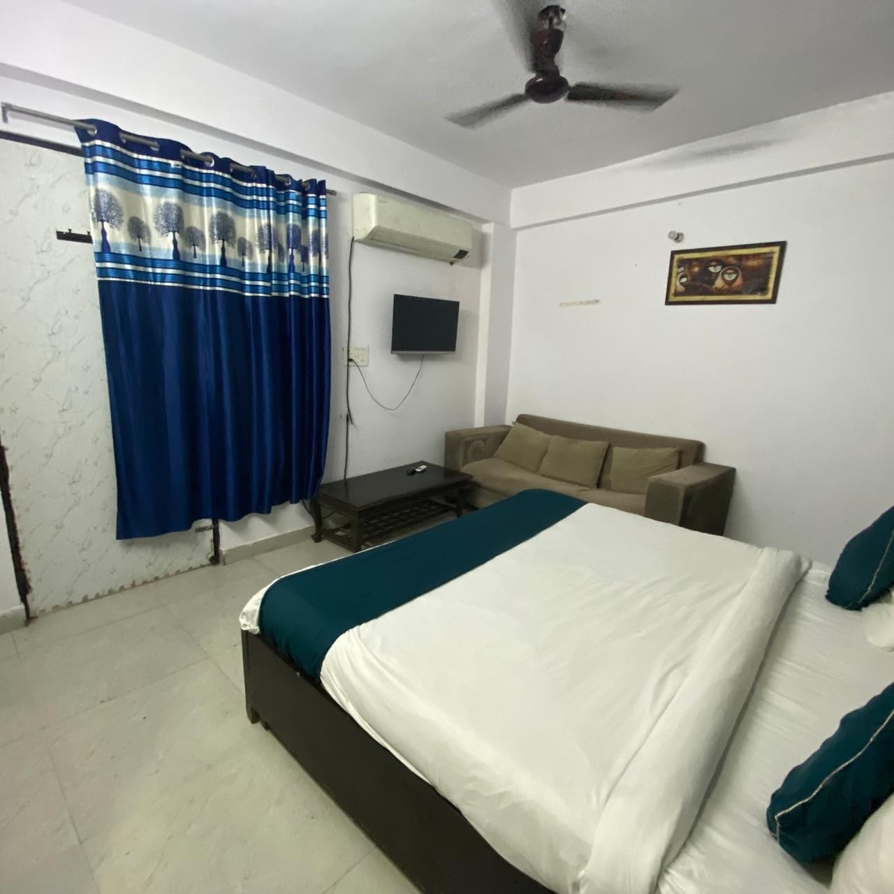 A bedroom with a bed, a sofa, a TV, and a ceiling fan.