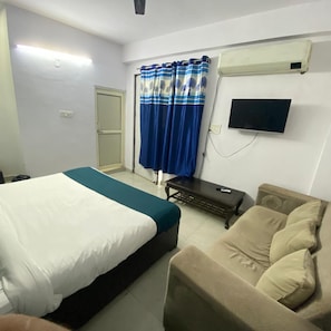 A hotel room with a bed, a sofa, a television, and curtains. - Roomshala 29 Silver Grand (Noida sec-49) (Noida)