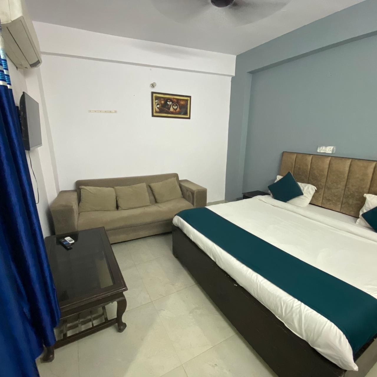 A bedroom with a bed, a sofa, a small table, and a wall-mounted TV.