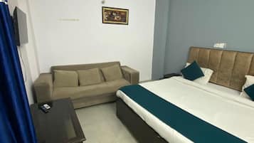 A bedroom with a bed, a sofa, a small table, and a wall-mounted TV.