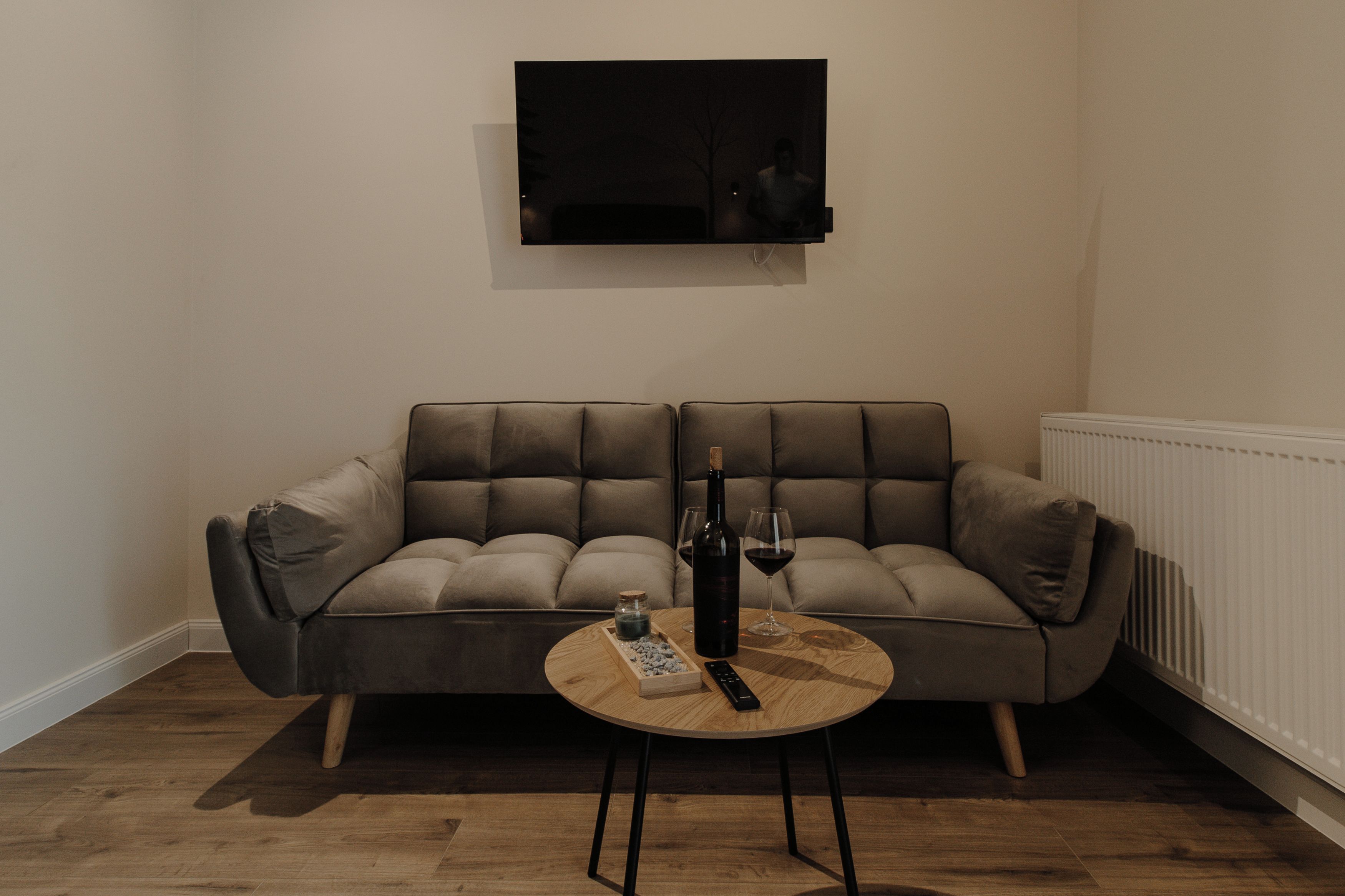 Uma sala de estar moderna com um sofá cinzento, uma mesa de centro de madeira, uma garrafa de vinho e um controle remoto.