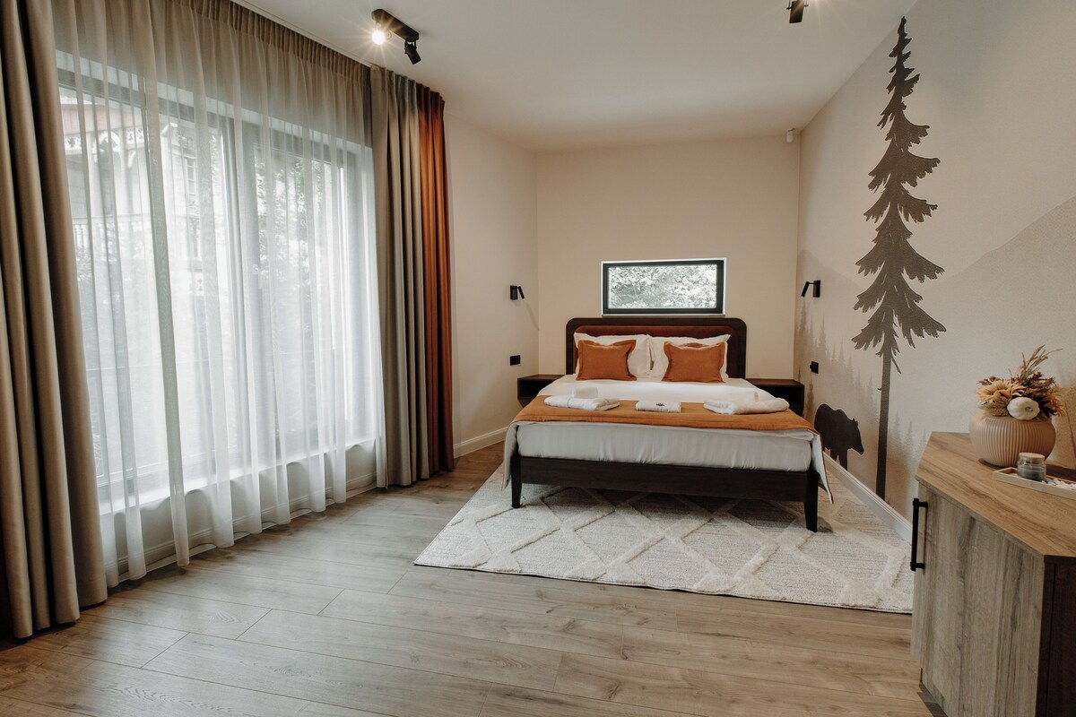 A bedroom with a bed, a window, a wall with a tree mural, and a wooden dresser.