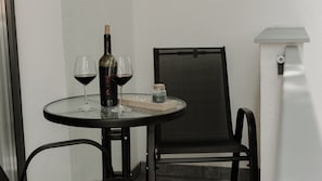 Una mesa redonda pequeña con una botella de vino, dos copas de vino tinto, una vela y un frasco pequeño sobre una superficie de vidrio.