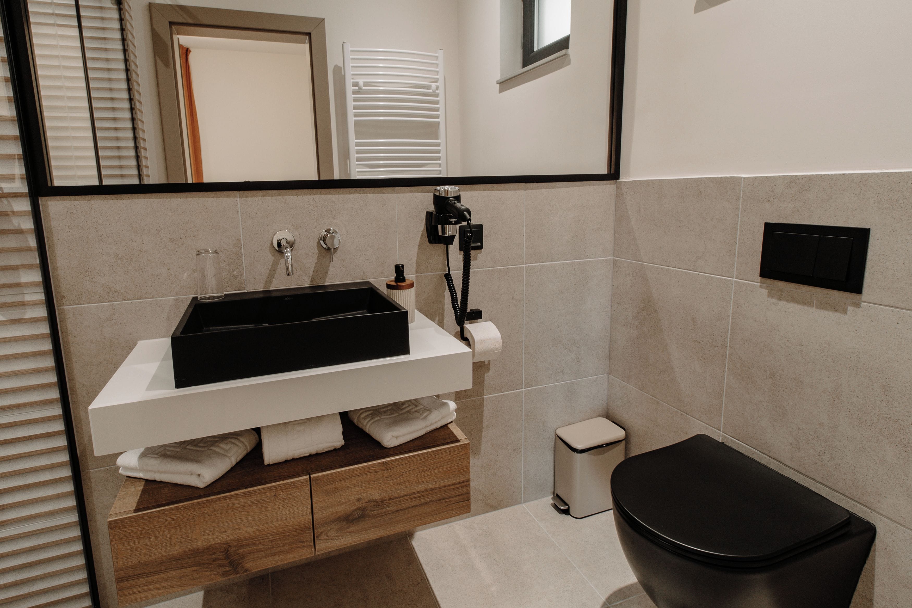 Un bany modern amb un lavabo blanc, un vàter negre i un petit safataixa.