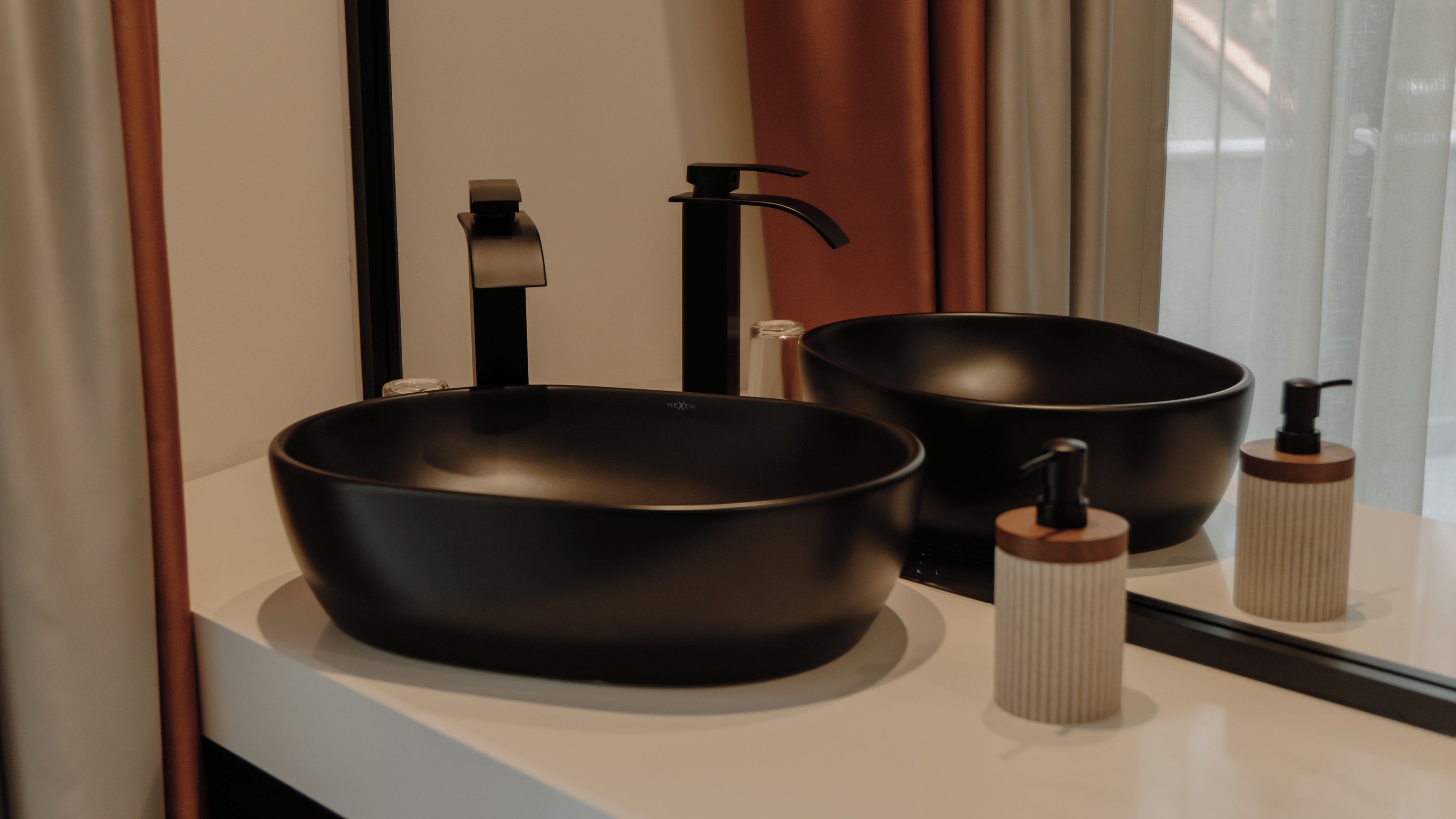 A bathroom with two black vessel sinks, a faucet, and a soap dispenser on the counter.