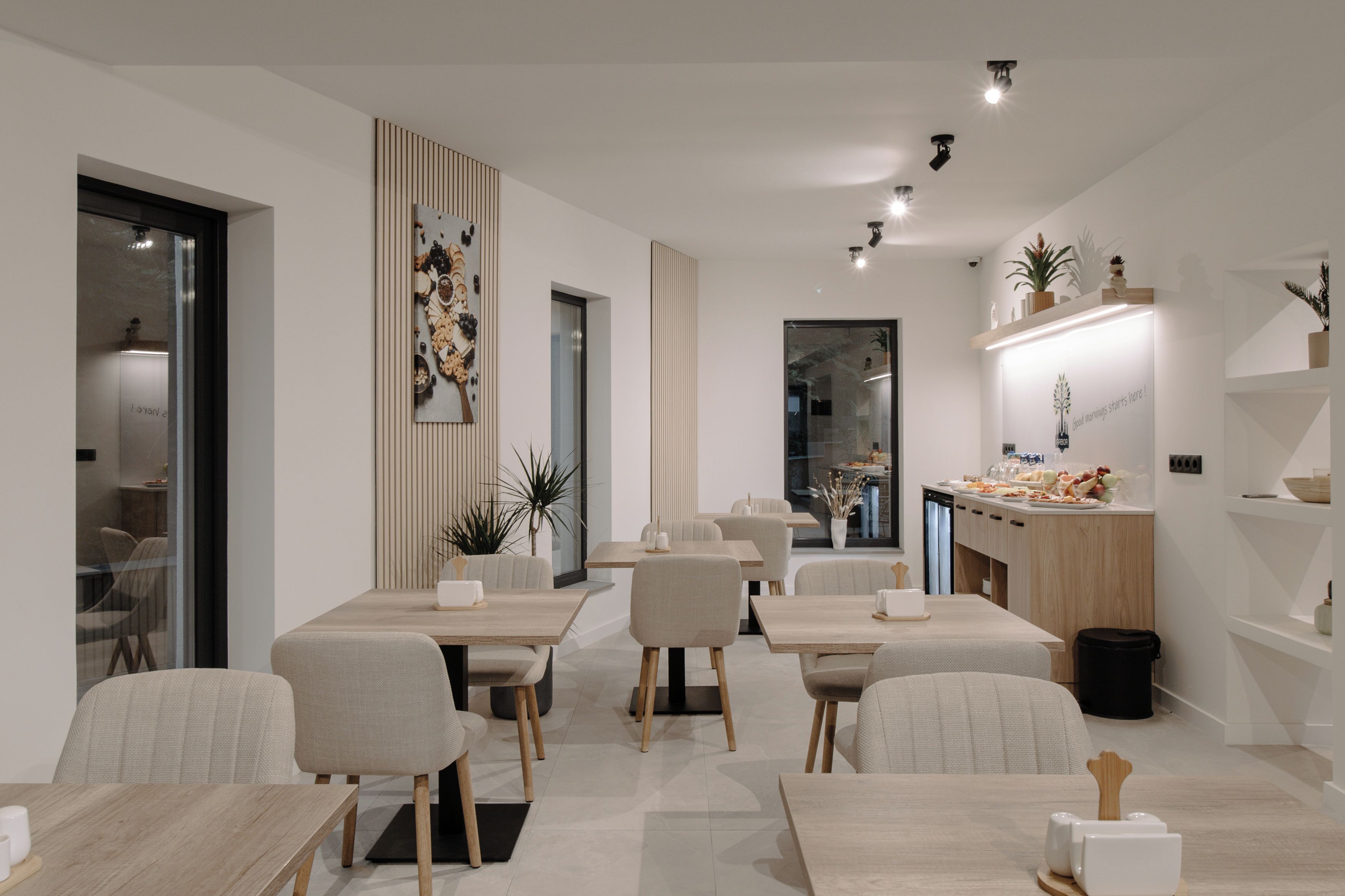 Un espace repas moderne avec plusieurs tables et chaises, un comptoir de cuisine où sont disposés des aliments et un élément décoratif mural.
