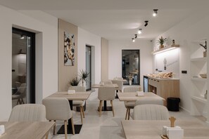 A modern dining area with multiple tables and chairs, a kitchen counter with food items, and a decorative wall piece. - Arbor Hotel (Sovata)
