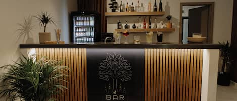 A bar area with a wooden counter, a refrigerator stocked with beverages, and a sign that reads 'BAR Where evenings begin.'