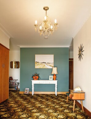 Quarto com lustre, pintura na parede, mesa consola com abajur e tapete estampado.