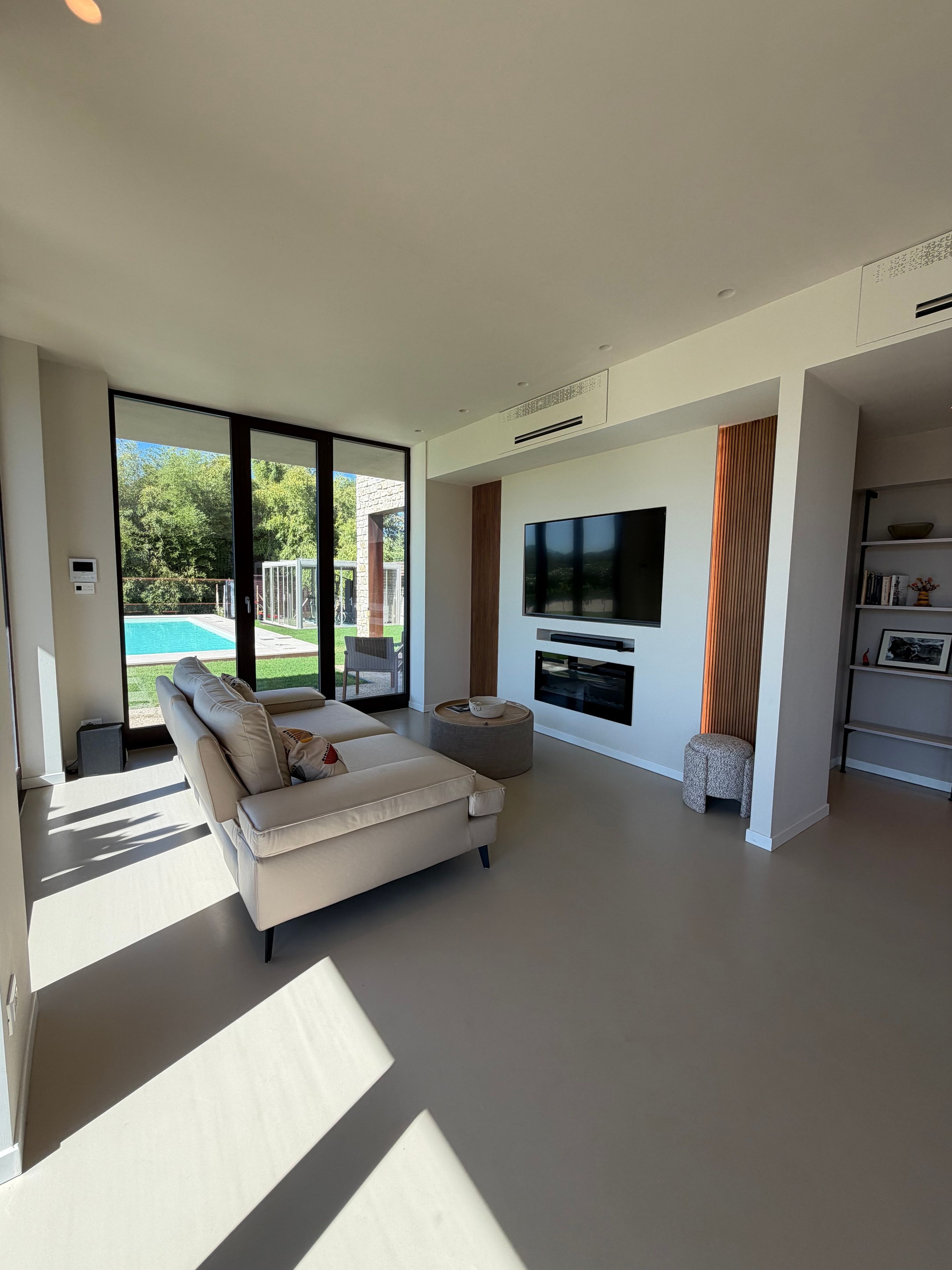 Un soggiorno moderno con un divano, una televisione a schermo piatto e vista su una piscina.