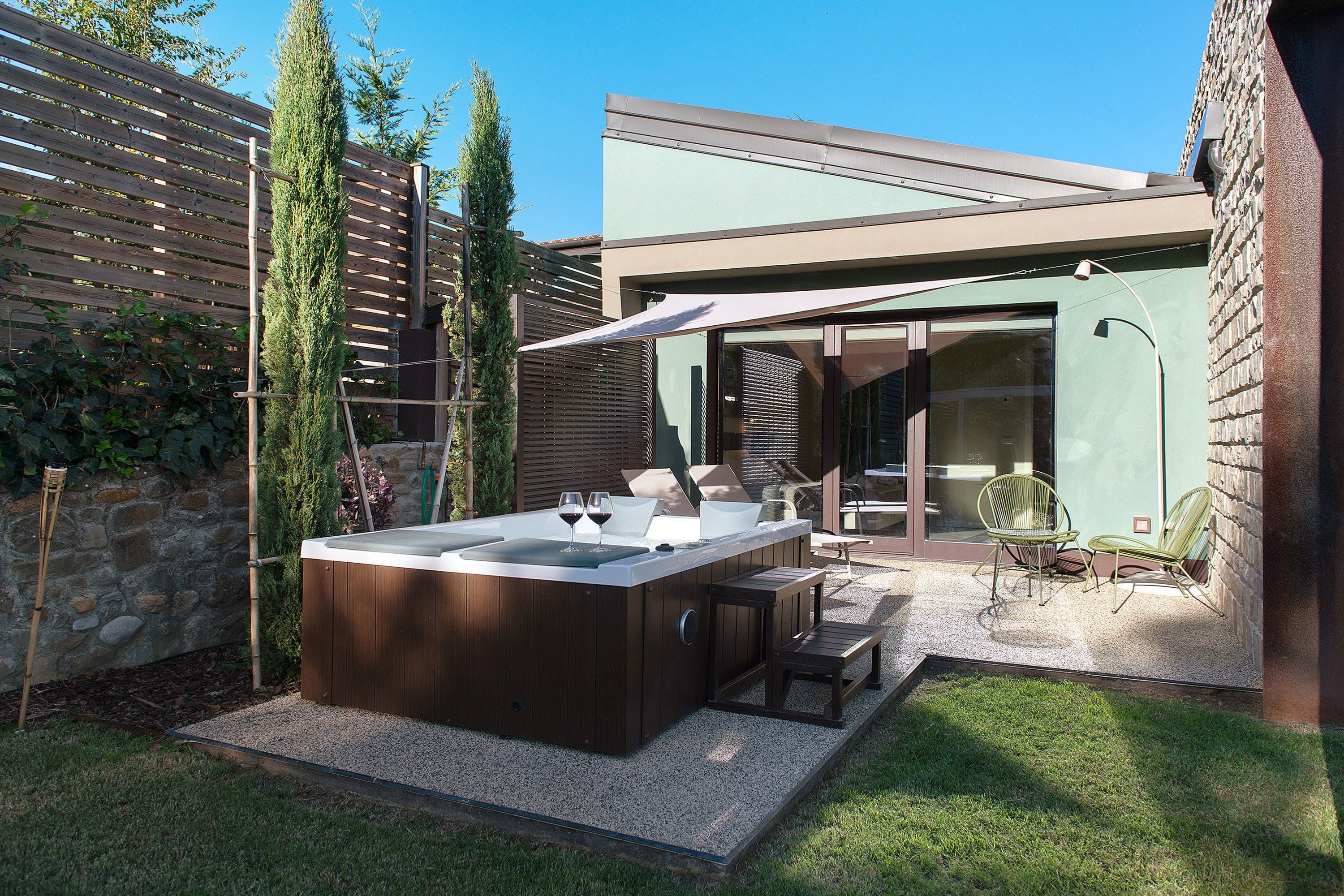 Ein Whirlpool mit Holzterrasse, Steinwand und Rasenfläche mit Gartenmöbeln.