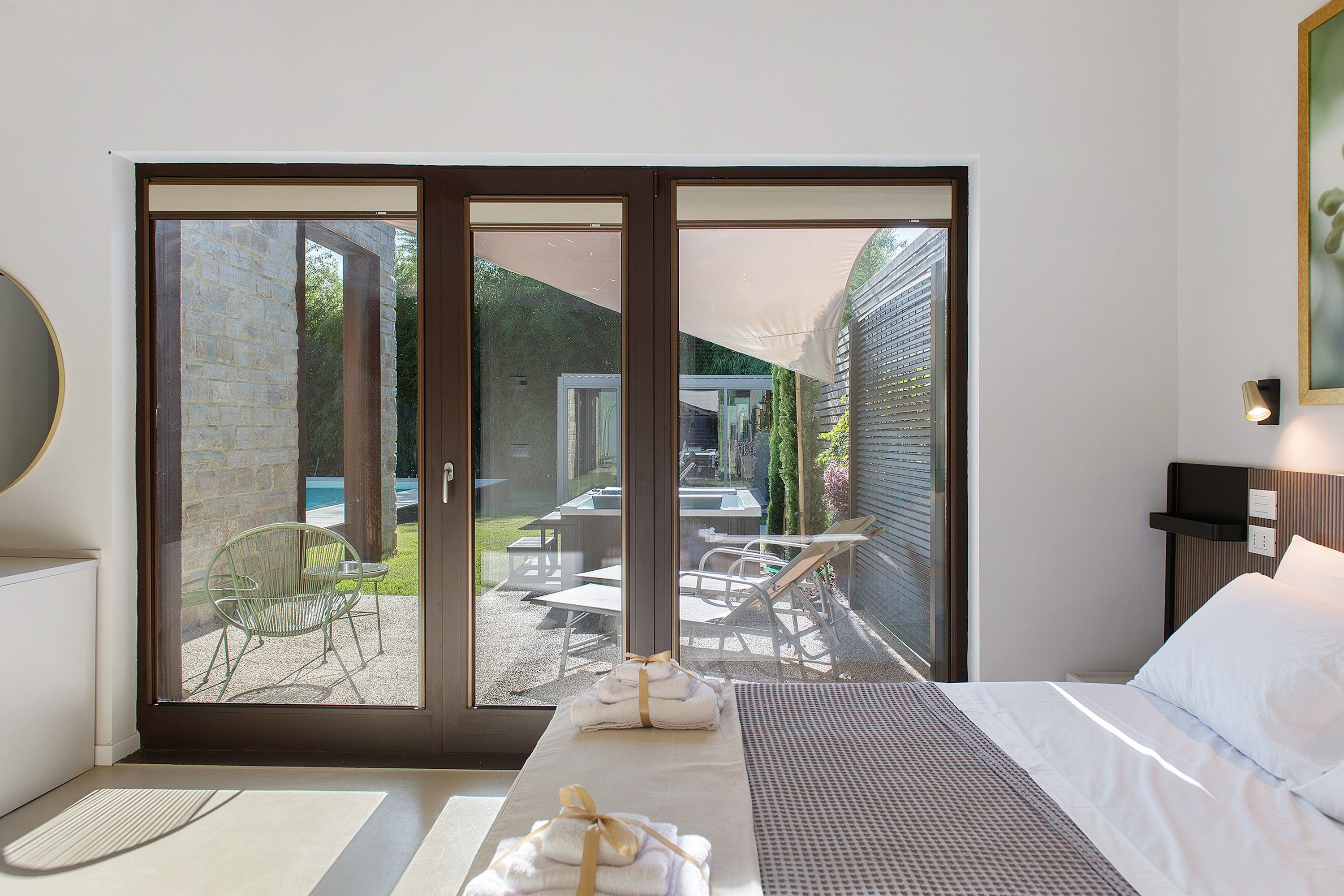 A hotel room with a bed, a table with chairs, and a view of an outdoor area with tables and chairs.