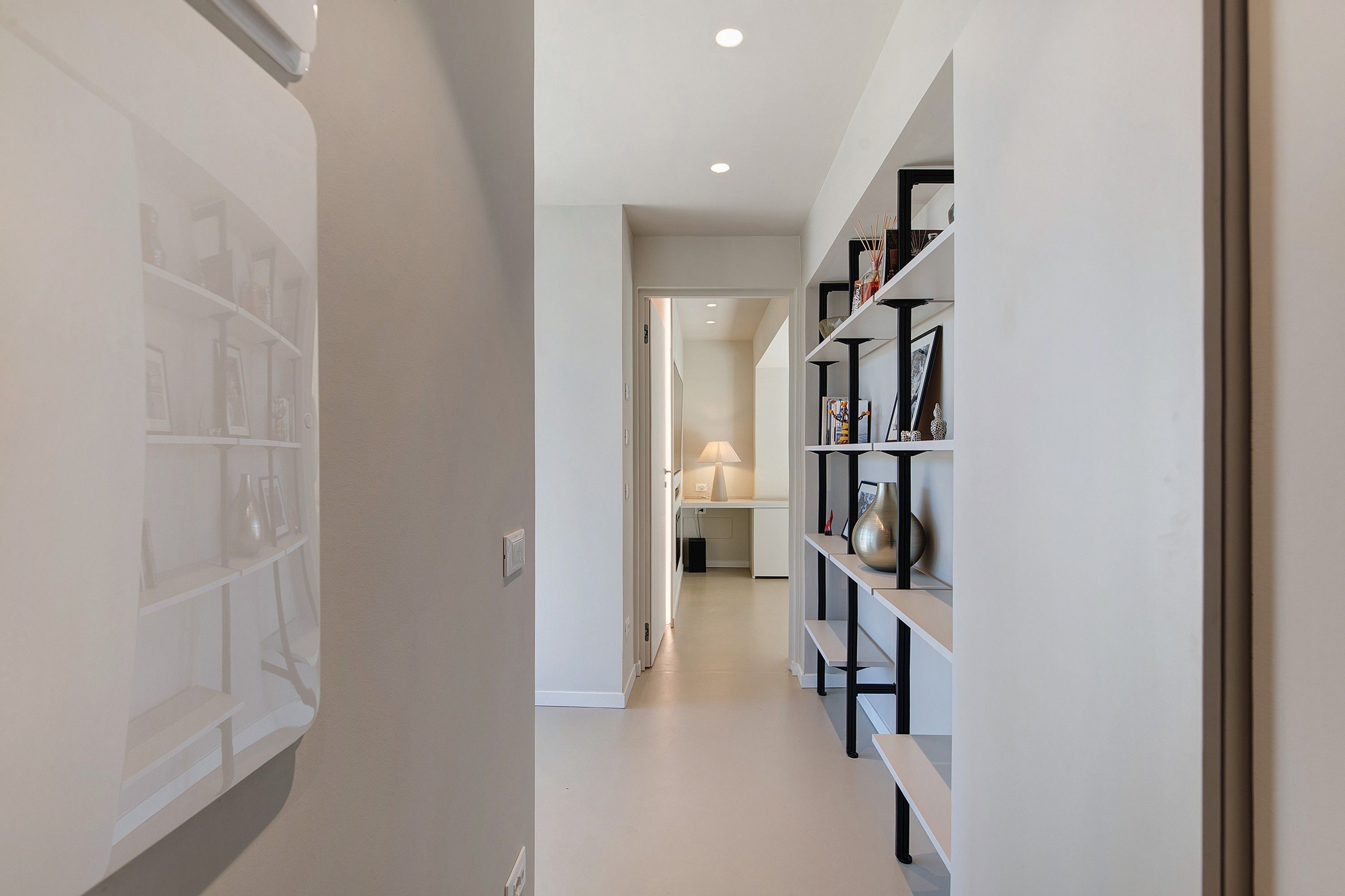 A hallway with a bookshelf, a door leading to another room, and a lamp.